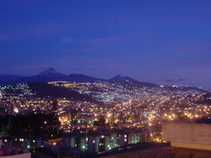 Quito at dusk. In the background, from left to right, are the volcanoes Cotopaxi, Pasochoa and Rumi&ntilde;ahui.