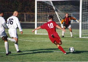 The striker (wearing a red shirt) has run past the defender (in white shirt) and is about to take a shot at the goal, while the goalkeeper positions himself to attempt to stop the ball.