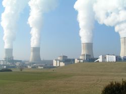 A nuclear power station. Non-radioactive water vapor rises from the hyperboloid shaped cooling towers. The nuclear reactors are inside the cylindrical containment buildings.