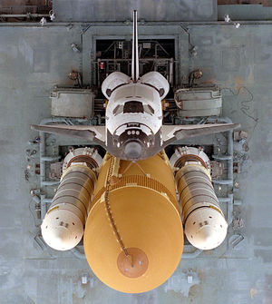The Shuttle sits atop the Mobile Launcher Platform (MLP). It consists of Orbiter (on top), External Tank (at center), and Solid Rocket Boosters (to the right and left of External Tank). Two Tail Service Masts (TSMs) to the either side of the Orbiter's tail provide  umbilical connections for propellent loading and electrical power. 