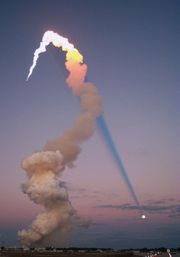 Shuttle launch of Atlantis at sunset in 2001. The sun is behind the camera, and the plume's shadow intersects the moon across the sky.