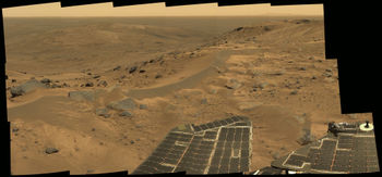 Spirit's "postcard" view from the summit of Husband Hill. It appears to be a windswept plateau strewn with rocks, small exposures of outcrop, and sand dunes. The view is to the north, looking down upon the "Tennessee Valley". this approximate true-colour composite spans about 90 degrees and consists of 18 frames captured by the rover's panoramic camera.